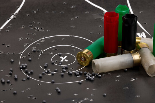 Empty fired shotgun shell and lead pellets on bull eye paper target background