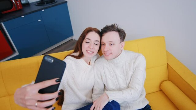 a young married couple at home. They sit on the couch and take selfies or talk on video communication