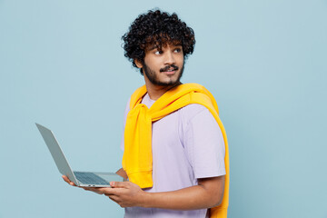 Blithesome charismatic fun young bearded Indian man 20s years old wears white t-shirt hold use work on laptop pc computer looking behind isolated on plain pastel light blue background studio portrait.