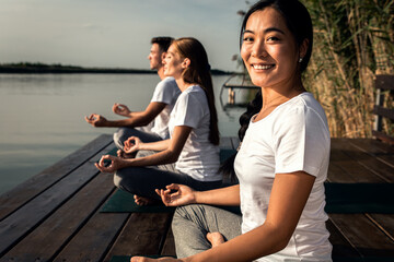 Group of people doing yoga exercises by the lake at sunset.