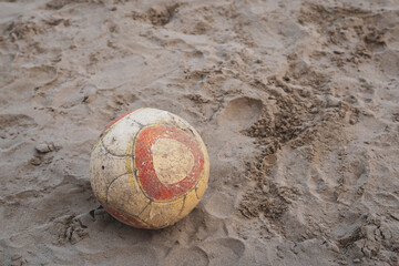 Old vintage ball abandoned on a beach. Beach volleyball on the sand. Used items and littering. Isolated dirty football item.