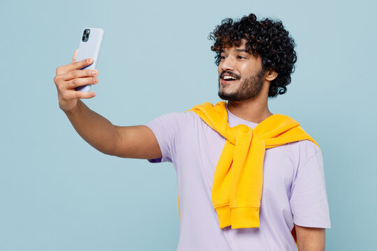 Fascinating young bearded Indian man 20s years old wears white t-shirt do selfie shot on mobile cell phone post photo on social network isolated on plain pastel light blue background studio portrait.