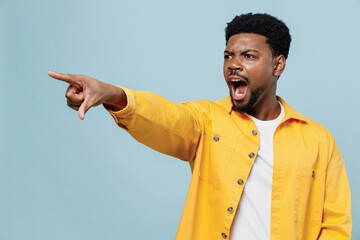 Young sad indignant strict angry man of African American ethnicity 20s in yellow shirt point index finger aside scream isolated on plain pastel light blue background studio. People lifestyle concept