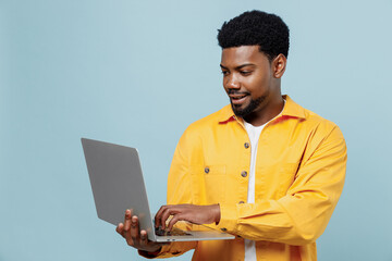 Young smiling happy man of African American ethnicity 20s wear yellow shirt hold use work on laptop...