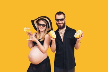 A bearded man and a pregnant girl in a bathing suit on a yellow background. Refreshing fruits and drinks