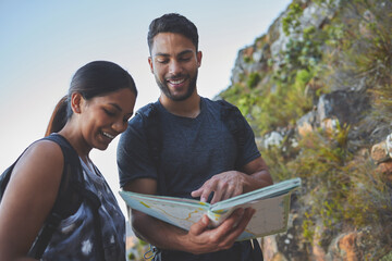 Maps are so helpful when hiking. Shot of a young couple using a guide book to complete a hike in a...
