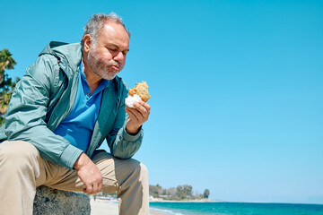 Bearded mature man at spring seaside eating hot palatable panzarotto (calzone pizza fried in hot...