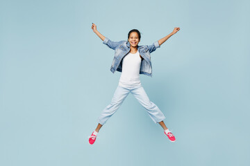 Fototapeta na wymiar Full size happy little kid teen girl of African American ethnicity 12-13 year old in denim jacket jump high with outstretched hands isolated on pastel plain light blue background. Childhood concept