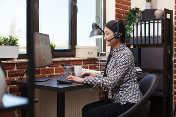 Asian sales representative with headset on call with potential customer. Helpline technical support operator answering client call regarding marketing agency online client platform.