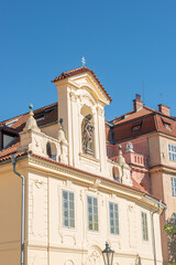 Ancient decorative top facade statue of priest, bishop with nimbus and holding a cross with crucified Christ at small church near Charles Bridge in Prague, Czech Republic, details, closeup.