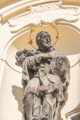 Ancient decorative top facade statue of priest, bishop with nimbus and holding a cross with crucified Christ at small church near Charles Bridge in Prague, Czech Republic, details, closeup.