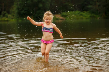Little cute girl have fun playing with a spray of water in the river at summer. copy space