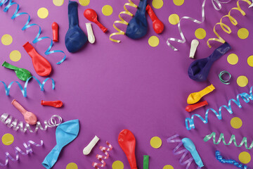 Frame of colorful serpentine streamers and other party accessories on purple background, flat lay. Space for text