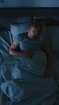 Top View of a Young Man in Bed at Night Having Terrible Nightmare, He Wakes Up Scared and Covered in Sweat. Video Footage with Vertical Screen Orientation