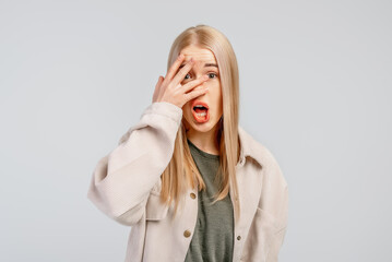 Portrait of shocked young blonde woman covering face with hand, hear bad news, problem trouble, wears casual clothes, stands against grey background. Body language concept