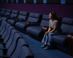 Caucasian red-haired woman sits on the last row in a cinema in an empty hall. The girl is watching a movie alone.