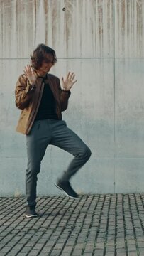 Cheerful and Happy Young Man with Long Hair Actively Dancing While Walking Down the Stairs. He's Wearing a Brown Leather Jacket. Vertical Screen Orientation Video