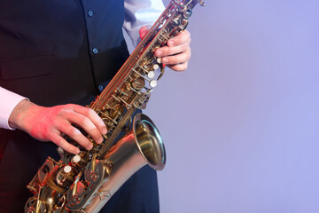 Fototapeta na wymiar Man in elegant outfit playing saxophone on color background, closeup. Space for text