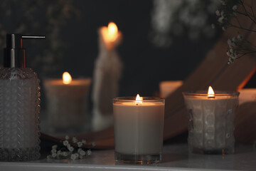 Beautiful burning candles and gypsophila flowers on white table near mirror indoors.