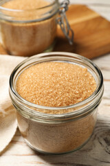 Glass jar with brown sugar on white wooden table, closeup