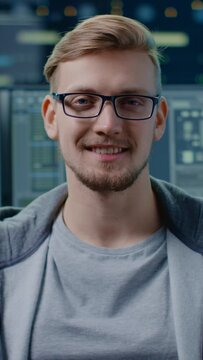 Portrait of a Smart and Handsome IT Specialist Wearing Glasses Smiles at the Camera. In the Background Personal Computers with Screens in Data Center. Vertical Screen Orientation Video