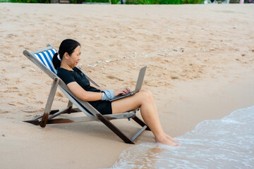 on vacation you have to do your work too. Asian woman sitting on a beach chair using his Notebook...