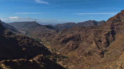 Beautiful aerial panoramic view of the rugged mountains in southern Gran Canaria, Canary Islands, Spain on sunny day with blue sky with winding road.