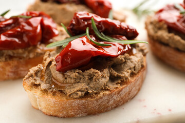 Slices of bread with delicious pate, sun dried tomatoes and rosemary on white board, closeup
