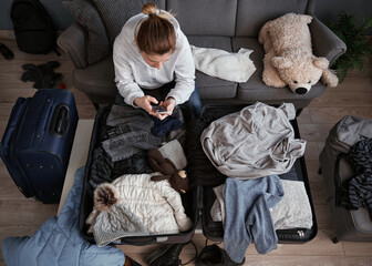 A woman is ready to leave her house and packing things in a suitcase. The woman looks into the...