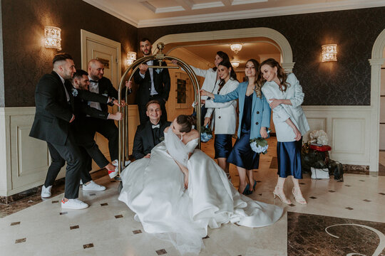 Joyful moment on the wedding of the young couple. Cheerful and fun groom with bride, bridesmaids and groomsmen posing in hotel