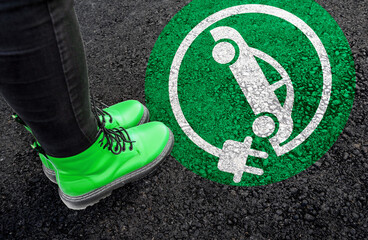 a woman with a boots is standing next to electric car sign on road asphalt  - obrazy, fototapety, plakaty