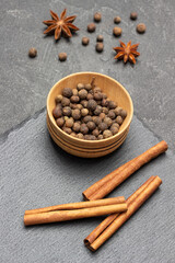 Allspice in wooden bowl and cinnamon sticks on stone board.
