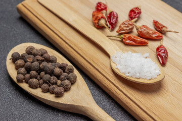Allspice in wooden spoon. Pods of red pepper and salt blackboard