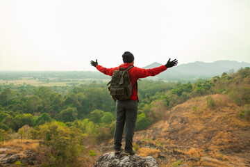 Asian young man conquers the peak success in life goals. Young asian man mountaineering wearing jacket walking at outdoor. Hiker with backpack and trekking pole.