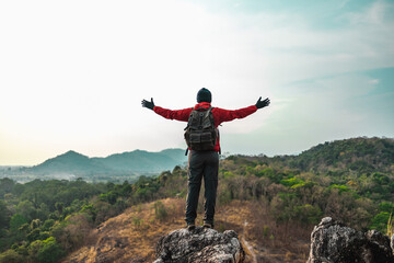 Asian young man conquers the peak success in life goals. Young asian man mountaineering wearing jacket walking at outdoor. Hiker with backpack and trekking pole.