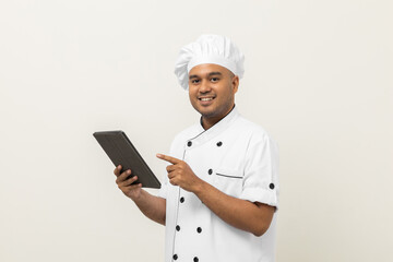 Young asian male chef holding digital tablet thinking to choose various delicious dish menu good taste for customer order. Online delivery food buying variety of dish