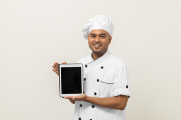 Young asian male chef holding digital tablet thinking to choose various delicious dish menu good taste for customer order. Online delivery food buying variety of dish