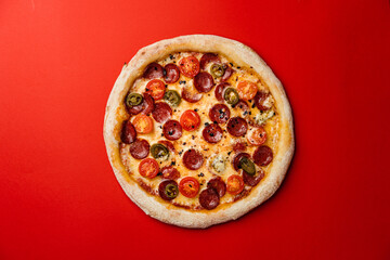 Pizza with smoked sausage, cherry tomatoes, dried chilli, jalapeno peppers and mozzarella. Red background. Top view. Copy space
