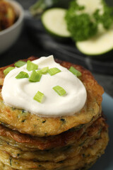 Delicious zucchini pancakes with sour cream and green onion on plate, closeup
