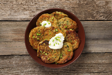 Delicious zucchini pancakes with sour cream and green onion on wooden table, top view