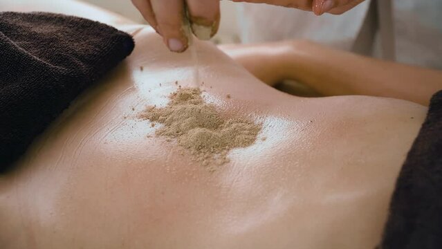 Masseuse pours cosmetic powder on slender belly of young woman with beautiful smooth skin. Concept of body care and alternative medicine