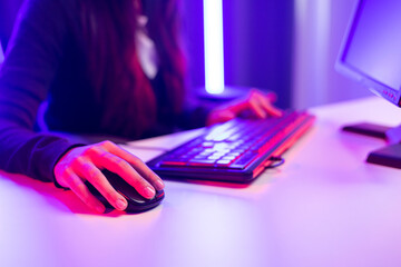Professional streamer. Close up hand woman holding mouse control playing video game on computer pc in living room. Female Streaming playing game online in dark room neon light
