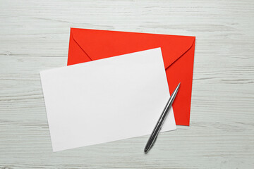 Envelope with blank paper card and pen on white wooden table, flat lay