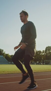 Athletic Fit Man in Grey Shirt and Shorts Hurdling in the Stadium. He is Jumping Over Barriers on a Warm Summer Afternoon. Slow Motion Tracking Shot. Vertical Screen Orientation Video