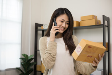 Startup Small business owner entrepreneur. Young asian business woman using mobile phone call receiving purchase order and check product on stock. E-commerce business and shopping online concept.