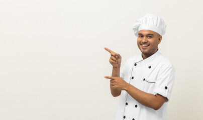 Smiling Young handsome asian man chef in uniform with hat standing pointing finger on isolated...