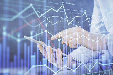 Double exposure of man's hands holding and using a digital device and forex graph drawing. Financial market concept.