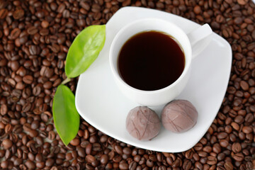 White cup of coffee with chocolate candy close up on coffee beand background