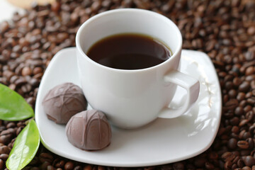White cup of coffee with chocolate candy close up on coffee beand background