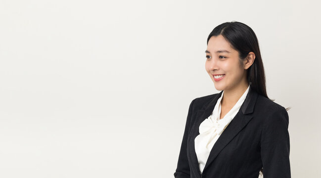 Young asian business woman smiling standing looking at blank space on isolated white background. Female around 25 in suit portrait shot in studio.